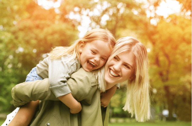 Cute young daughter on a piggy back ride with her mother.