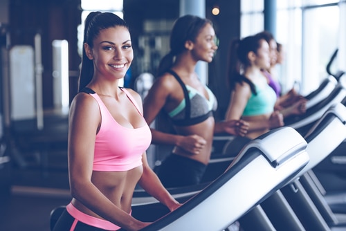 woman in sportswear looking at camera with smile while running on treadmill at gym