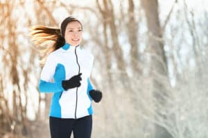 Female jogging in winter forest wearing warm sporty clothing and gloves.